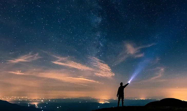 Guy at sunset holding a bright flashlight to the starry skies