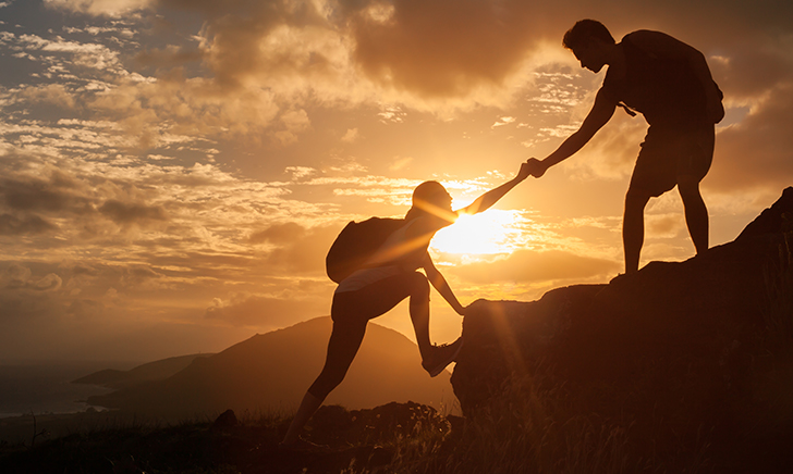 Two hikers on a mountain side with one lending a hand