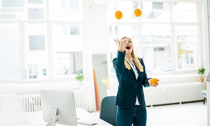A female executive juggles oranges in her office