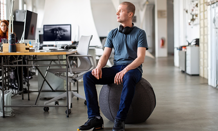 A colleague sits on a ball chair in an office setting