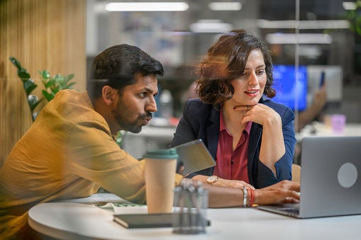 Businessman and woman working on laptop while sitting in office.