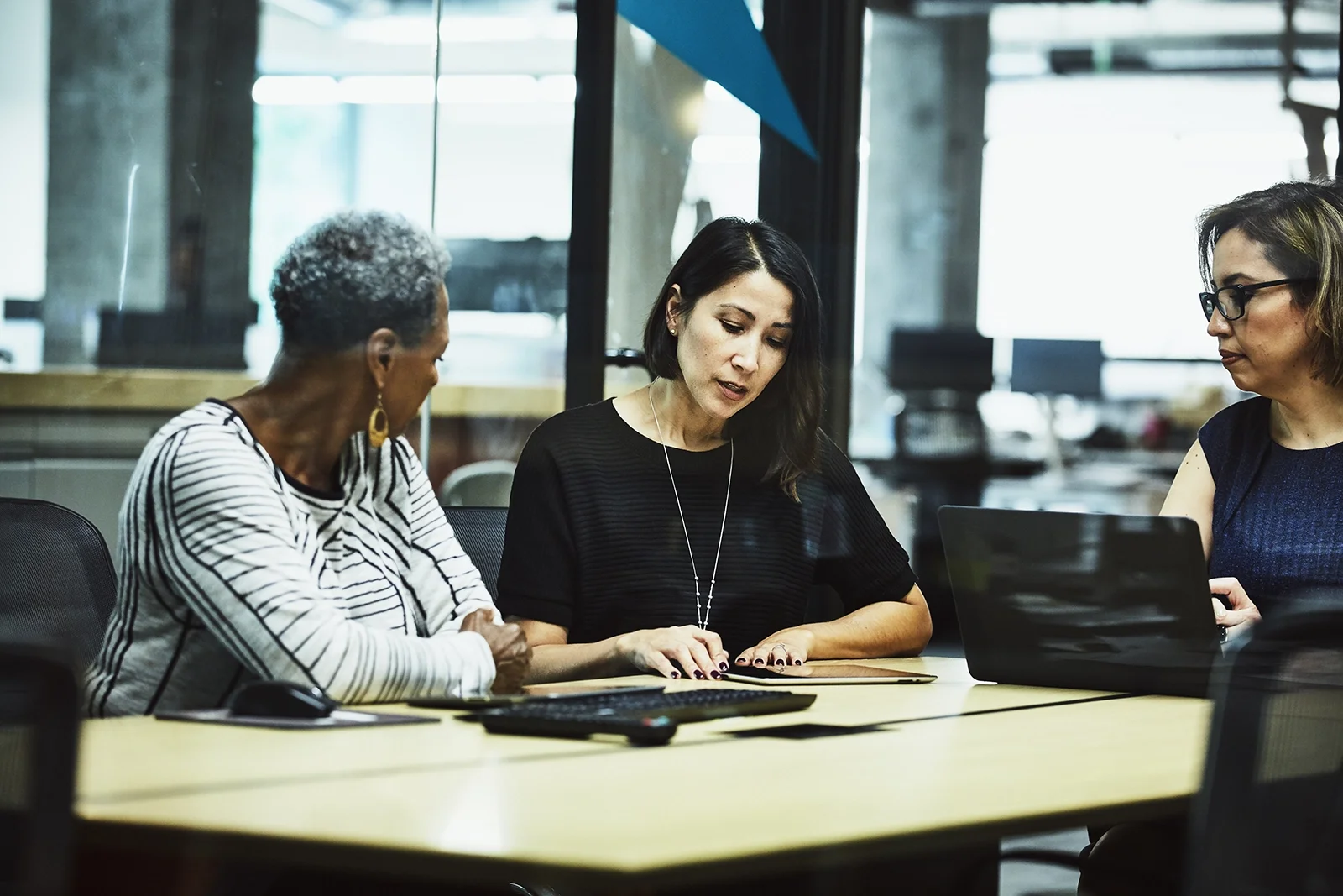 Three women sitting on a desk discussing.
