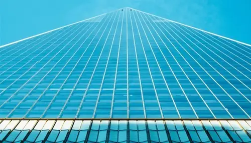 Upward view of a tall glass skyscraper with a grid pattern against a clear blue sky.