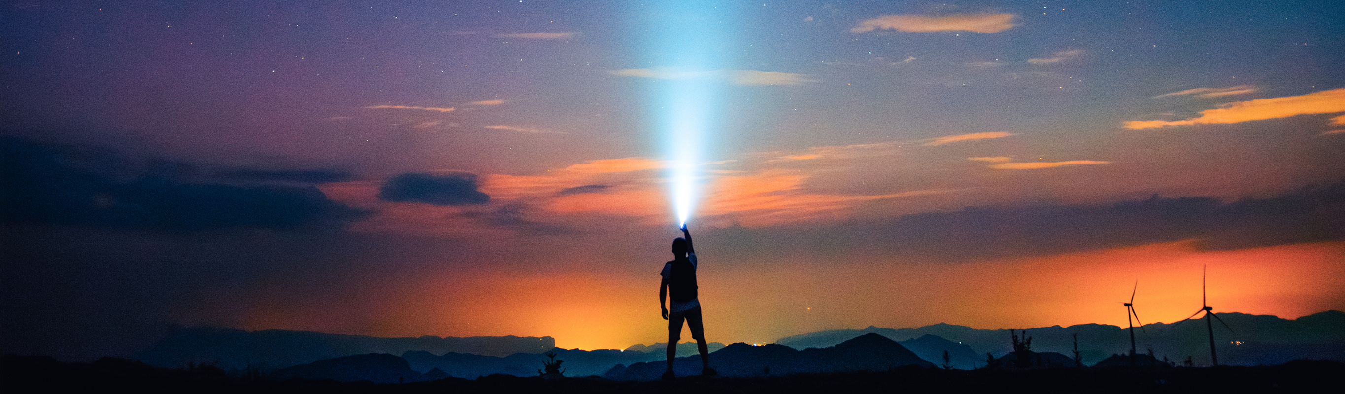 Silhouetted explorer shines flashlight into night sky