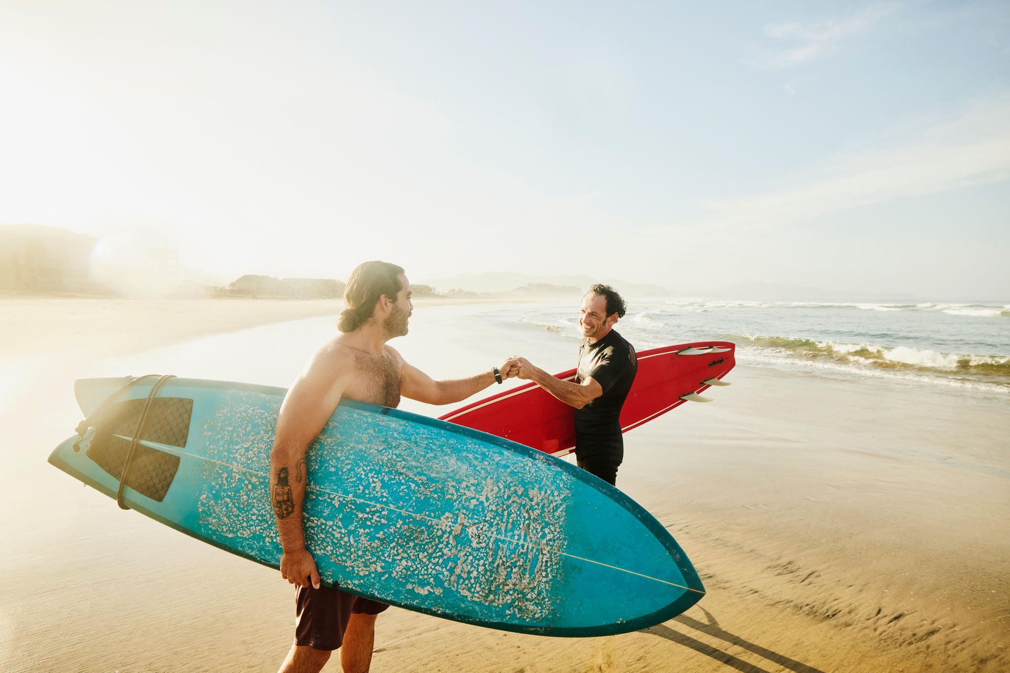 Medium wide shot of smiling friends fist bumping after early morning surf session