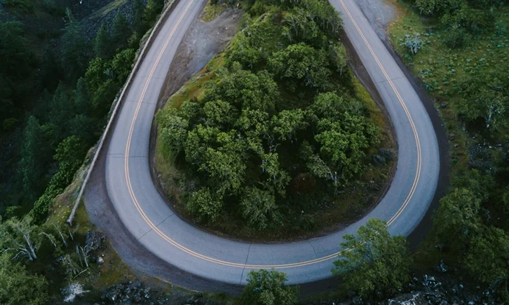 Aerial view of a sharp hairpin turn on a winding mountain road surrounded by dense green forest.