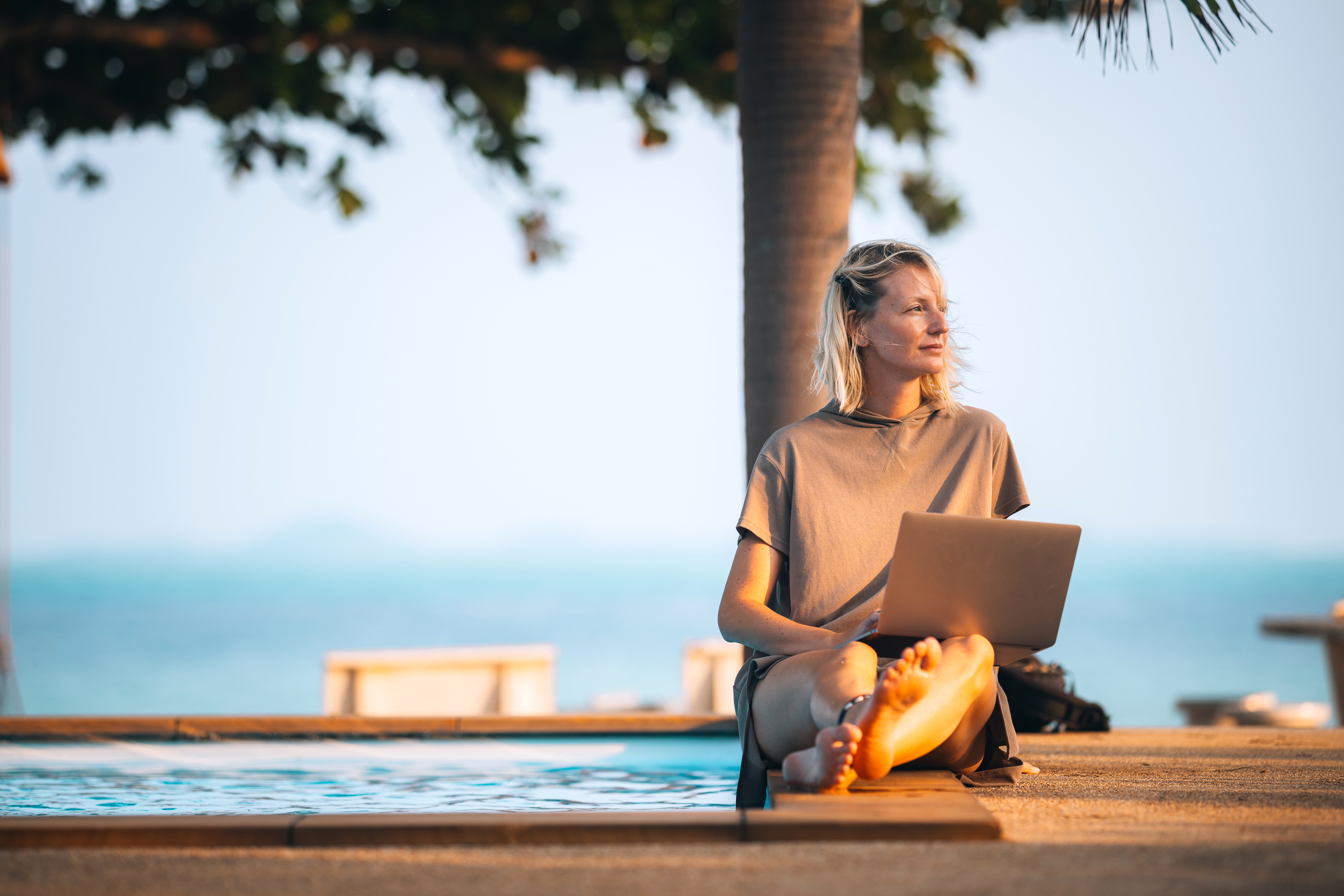 Woman wondering sitting by the pool with a laptop in her lap