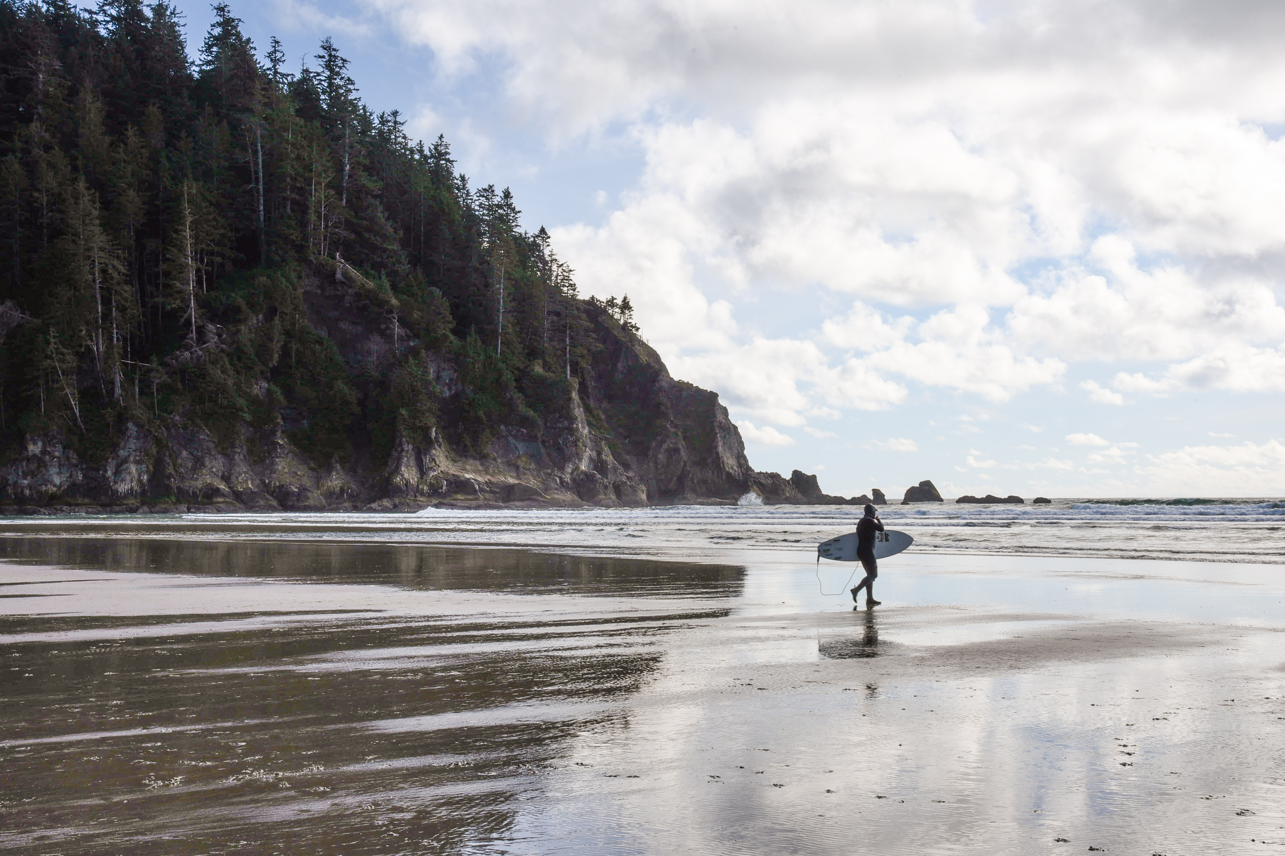 A guy is walking towards the sea with his surfing board