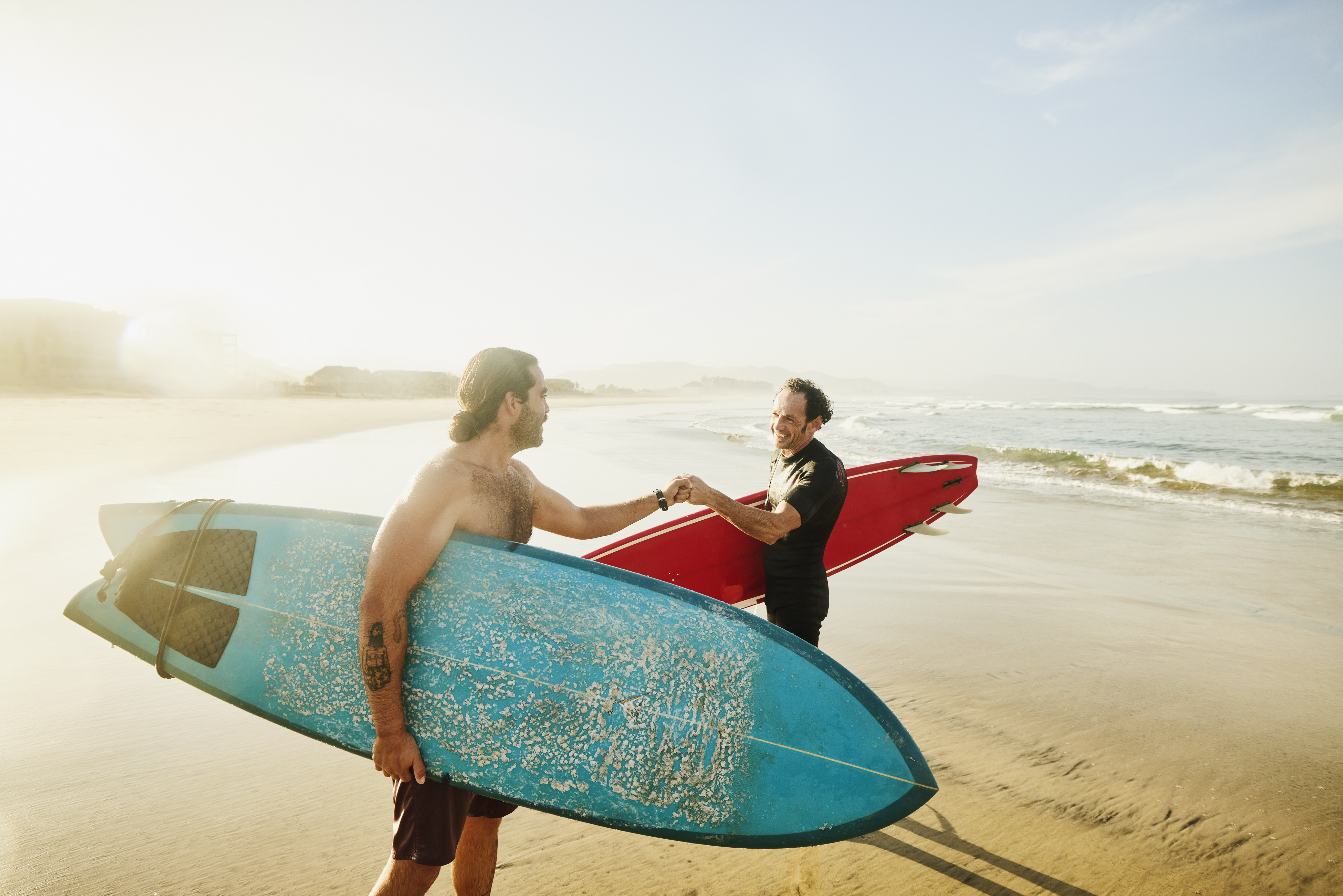 two people holding their surf boards and fist bumping by the sea