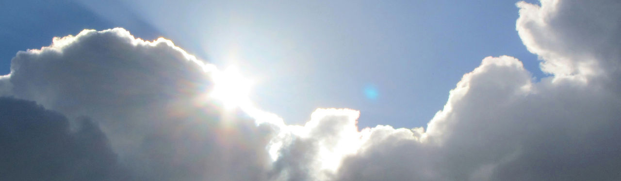 Bright sun in a blue sky with scattered white clouds.
