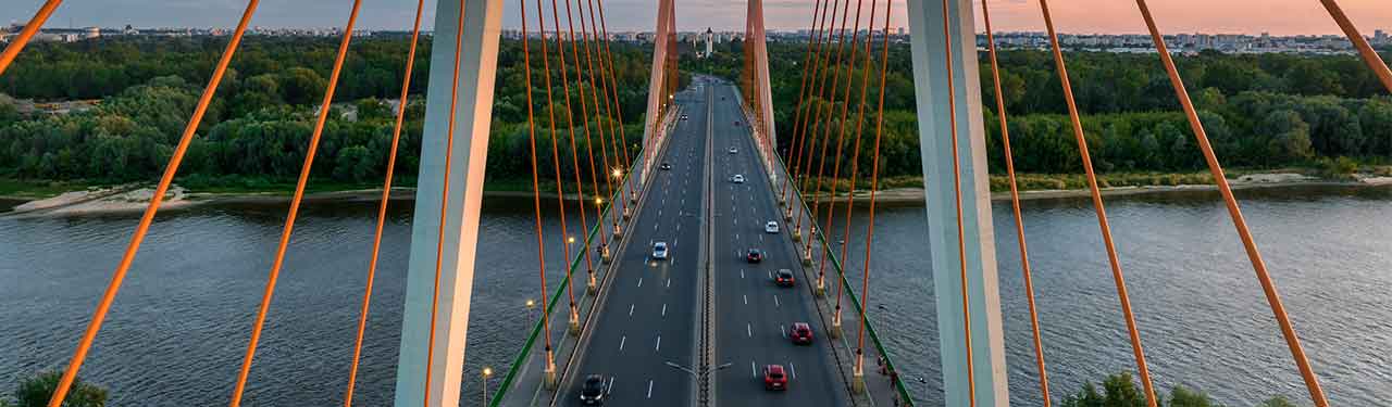 Suspension bridge with traffic over river at sunset